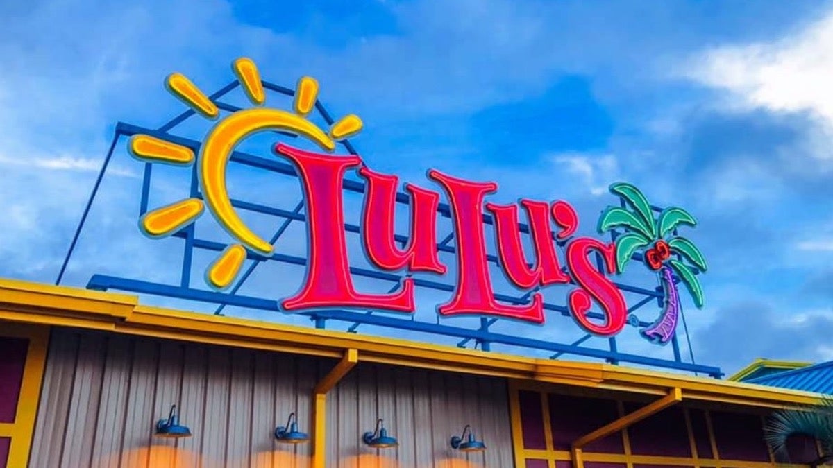 Bright pink LuLu's sign with a neon sun and palm tree with a blue sky behind it